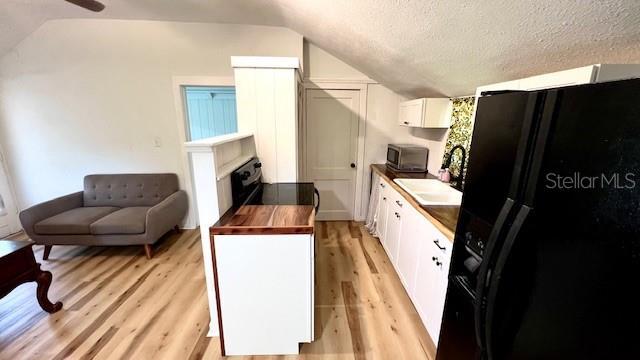 214 N New Hampshire Ave, Tavares, FL 32778 - kitchen featuring vaulted ceiling, black appliances, a sink, light wood-type flooring, and white cabinets