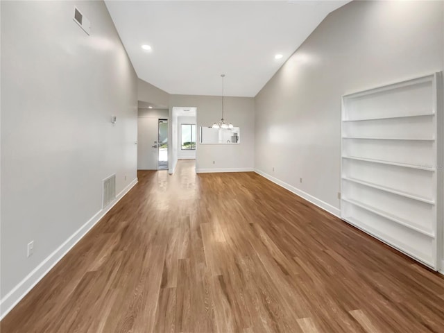 unfurnished living room with hardwood / wood-style floors, built in features, and a chandelier