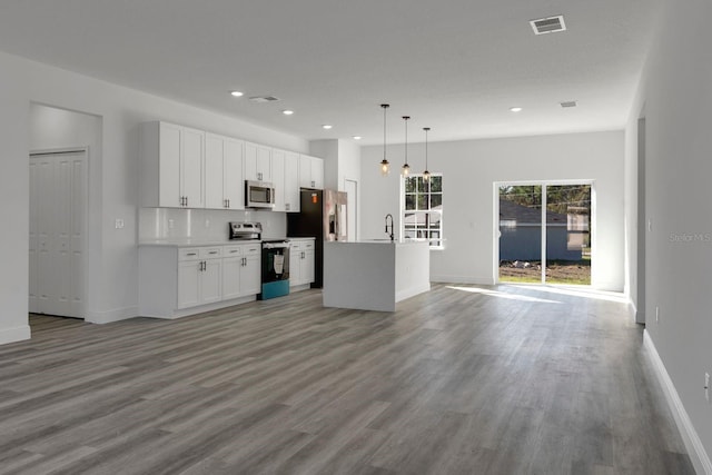 kitchen with white cabinetry, decorative light fixtures, a center island with sink, light wood-type flooring, and appliances with stainless steel finishes