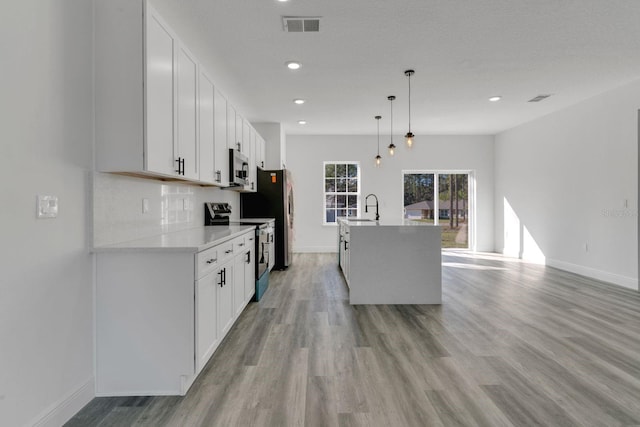 kitchen featuring sink, white cabinetry, stainless steel appliances, an island with sink, and decorative light fixtures