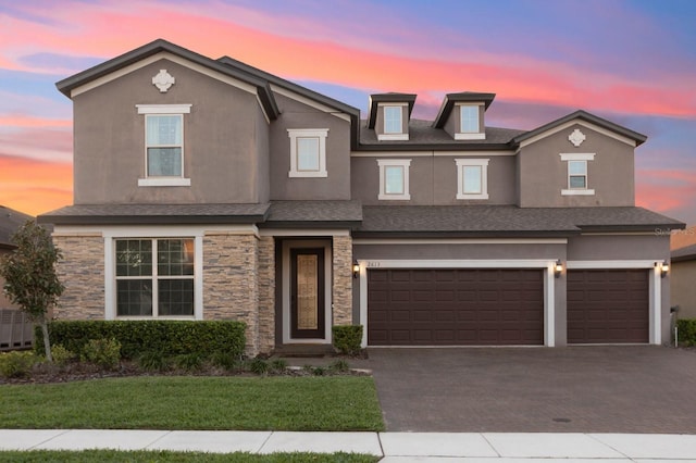 view of front of house with decorative driveway, stucco siding, a shingled roof, a garage, and stone siding