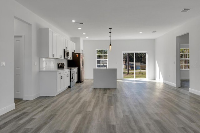 kitchen with tasteful backsplash, appliances with stainless steel finishes, pendant lighting, light hardwood / wood-style floors, and white cabinets