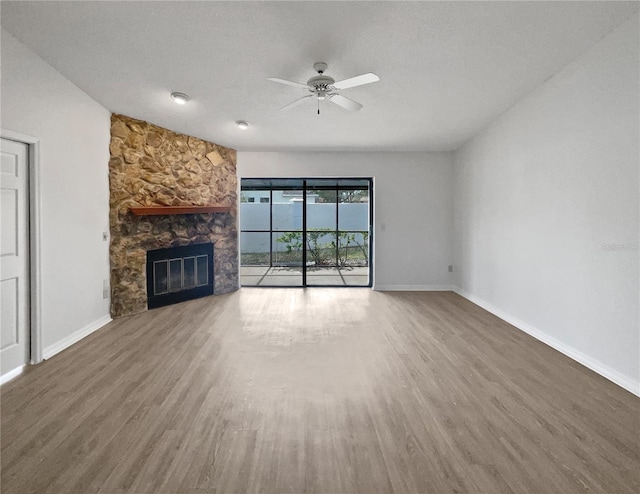 unfurnished living room with hardwood / wood-style flooring, a stone fireplace, a textured ceiling, and ceiling fan