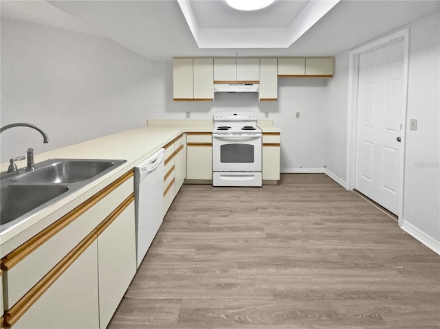 kitchen with cream cabinets, sink, a raised ceiling, white appliances, and light hardwood / wood-style floors