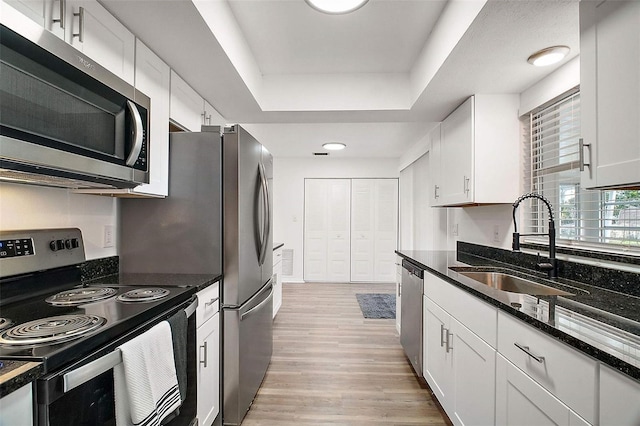 kitchen featuring sink, appliances with stainless steel finishes, a raised ceiling, dark stone counters, and white cabinets