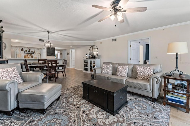 living room with crown molding, wood-type flooring, a textured ceiling, and ceiling fan with notable chandelier