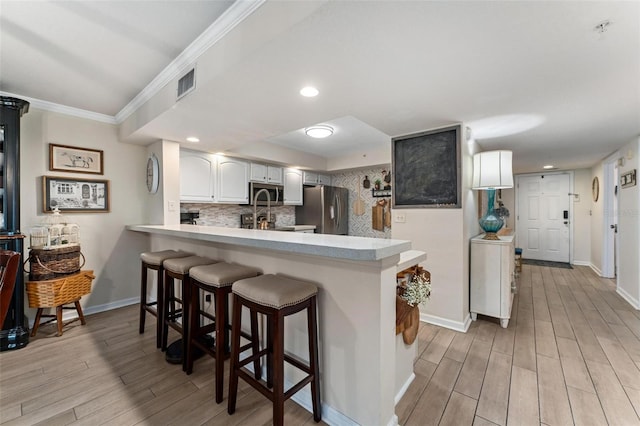 kitchen featuring appliances with stainless steel finishes, white cabinets, a kitchen breakfast bar, kitchen peninsula, and light wood-type flooring