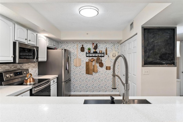 kitchen featuring sink, a textured ceiling, appliances with stainless steel finishes, decorative backsplash, and white cabinets