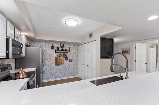 kitchen with appliances with stainless steel finishes, sink, white cabinets, dark wood-type flooring, and a textured ceiling