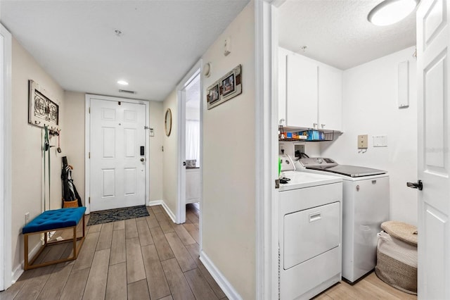 laundry area with cabinets, a textured ceiling, independent washer and dryer, and light hardwood / wood-style flooring