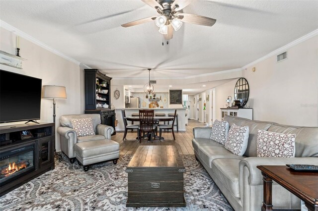 living room with crown molding, ceiling fan, dark hardwood / wood-style floors, and a textured ceiling