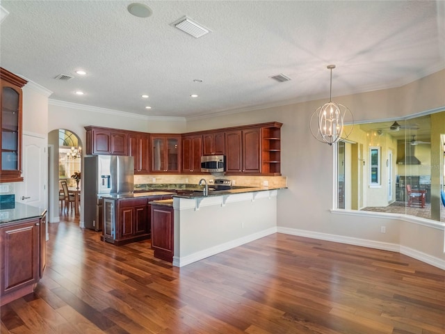 kitchen with hanging light fixtures, appliances with stainless steel finishes, dark hardwood / wood-style flooring, kitchen peninsula, and decorative backsplash