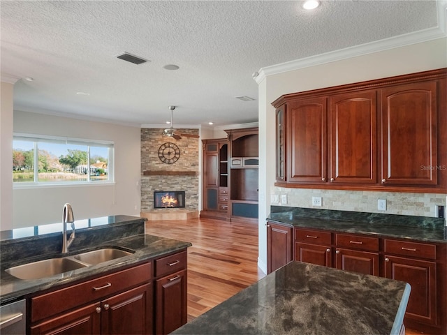 kitchen with sink, crown molding, light hardwood / wood-style flooring, a stone fireplace, and stainless steel dishwasher