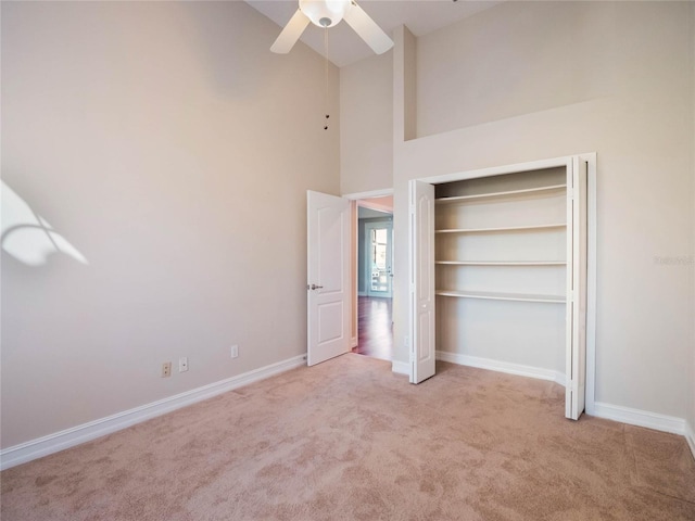 unfurnished bedroom featuring light colored carpet, ceiling fan, and a high ceiling