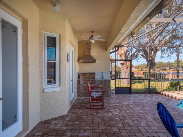 view of patio / terrace featuring ceiling fan, area for grilling, exterior kitchen, and glass enclosure