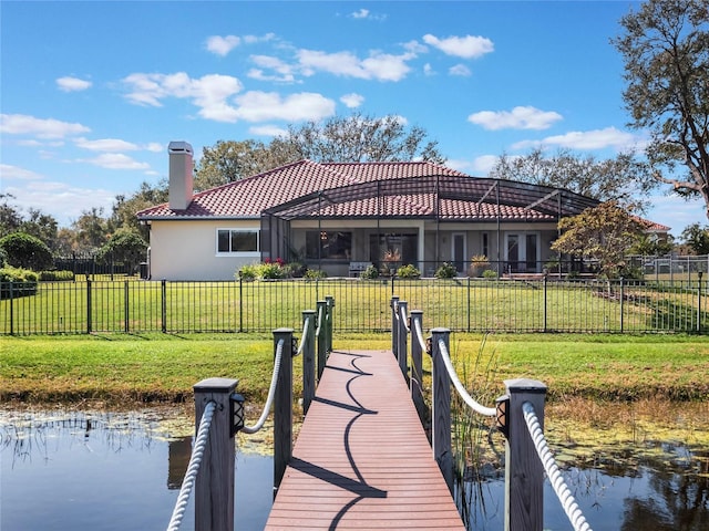 view of dock with a water view, glass enclosure, and a lawn