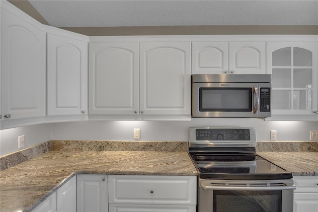 kitchen featuring white cabinetry, appliances with stainless steel finishes, a textured ceiling, and dark stone counters