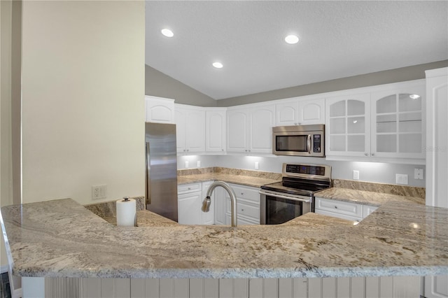 kitchen featuring white cabinetry, appliances with stainless steel finishes, kitchen peninsula, and vaulted ceiling