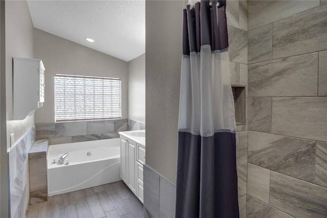 bathroom featuring a washtub, hardwood / wood-style floors, vanity, a textured ceiling, and vaulted ceiling