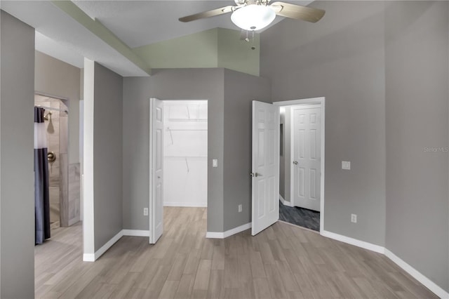 unfurnished bedroom featuring a spacious closet, vaulted ceiling, light wood-type flooring, a closet, and ceiling fan