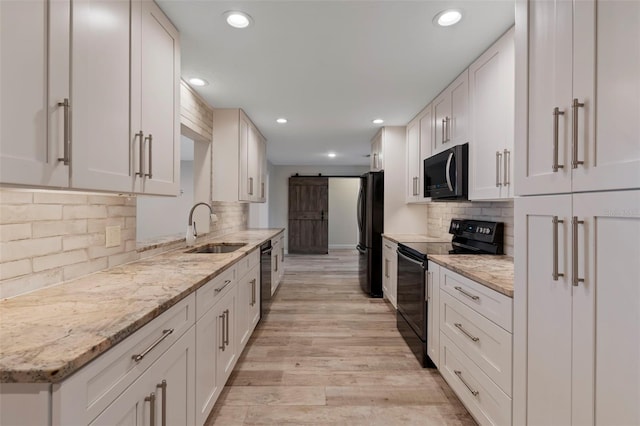 kitchen with sink, black appliances, light stone countertops, white cabinets, and a barn door