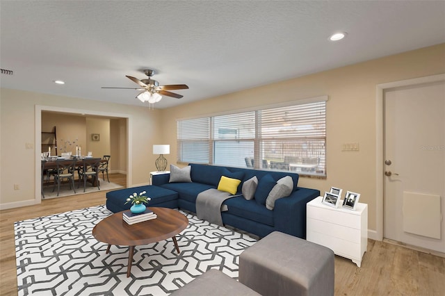 living room with ceiling fan, a textured ceiling, and light wood-type flooring