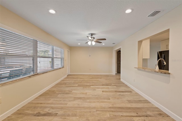 empty room featuring ceiling fan, sink, light hardwood / wood-style floors, and a textured ceiling