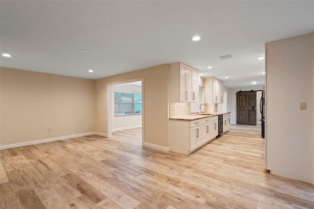 kitchen with a barn door, sink, backsplash, and light wood-type flooring