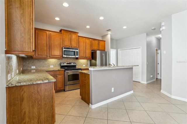 kitchen featuring a kitchen island with sink, stainless steel appliances, light stone counters, tasteful backsplash, and light tile patterned flooring