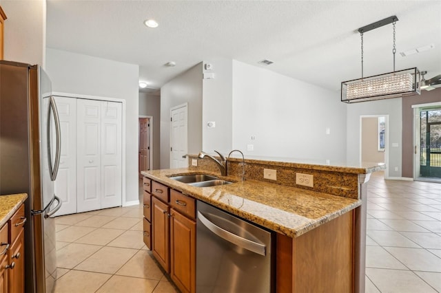 kitchen with sink, a kitchen island with sink, stainless steel appliances, light tile patterned flooring, and decorative light fixtures