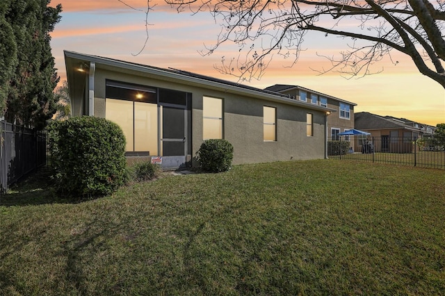 back house at dusk featuring a lawn