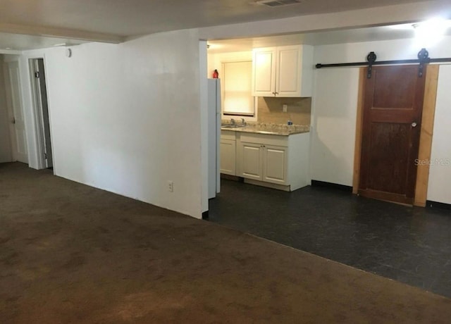 kitchen featuring white cabinetry, a barn door, and dark carpet