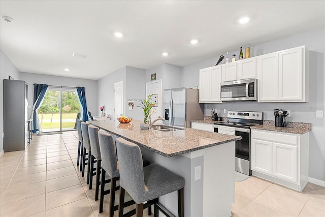 kitchen featuring light stone counters, stainless steel appliances, sink, and an island with sink