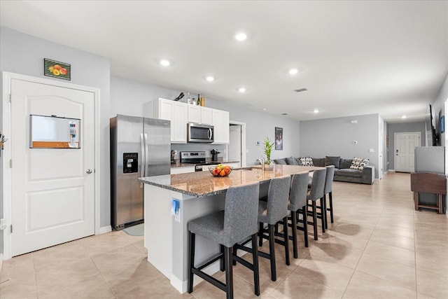 kitchen with light stone counters, a center island with sink, stainless steel appliances, visible vents, and a kitchen bar