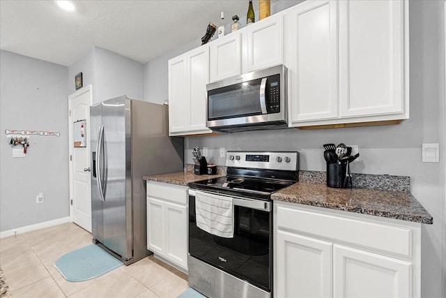 kitchen featuring stainless steel appliances, dark stone counters, white cabinetry, and light tile patterned floors