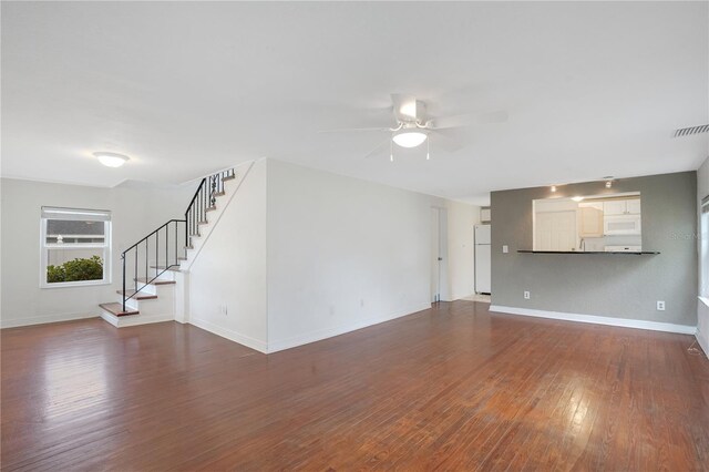 unfurnished living room featuring hardwood / wood-style floors, a ceiling fan, visible vents, baseboards, and stairs