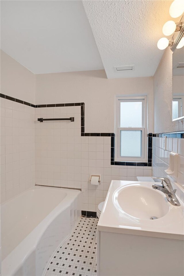 full bath featuring a bathing tub, a textured ceiling, tile walls, and toilet