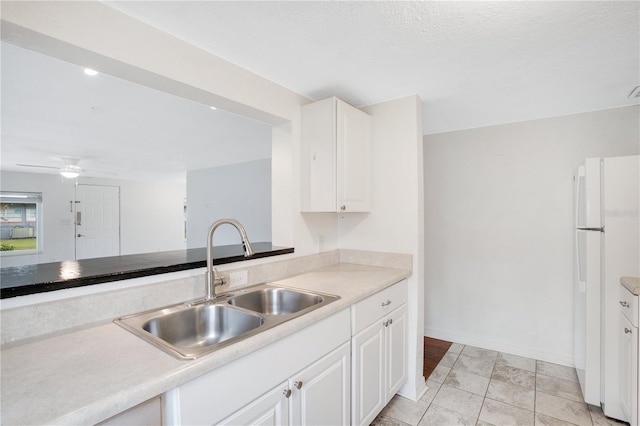 kitchen with a ceiling fan, freestanding refrigerator, a sink, light countertops, and white cabinetry