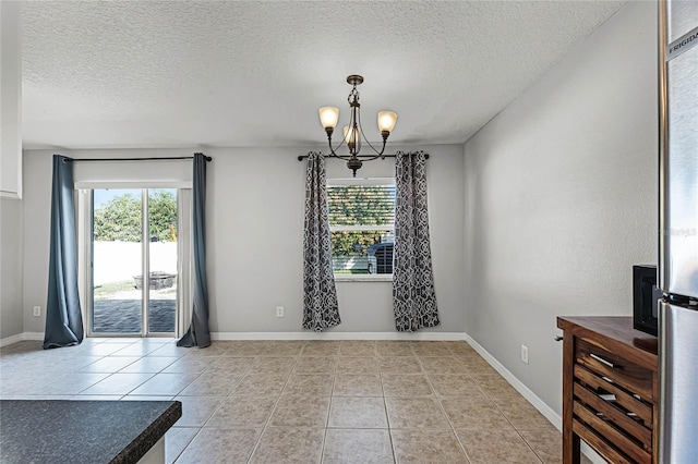 unfurnished dining area featuring a healthy amount of sunlight, light tile patterned floors, a textured ceiling, and a notable chandelier