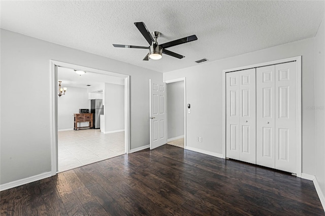 unfurnished bedroom featuring ceiling fan, wood-type flooring, stainless steel refrigerator, and a textured ceiling