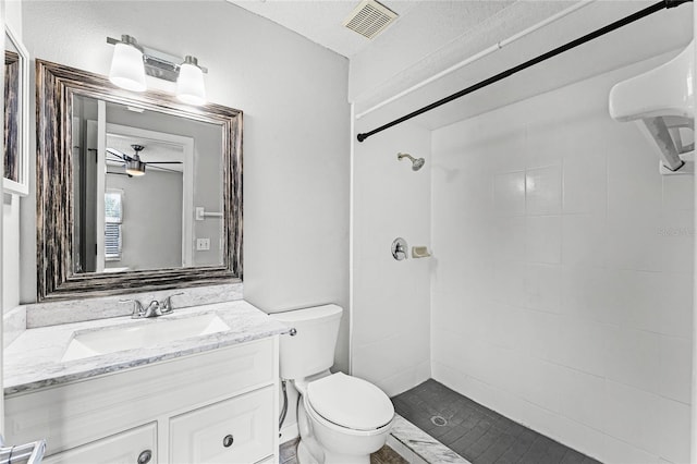 bathroom with vanity, tiled shower, ceiling fan, and toilet