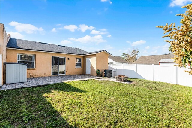 rear view of house with cooling unit, a yard, a patio, and a fire pit