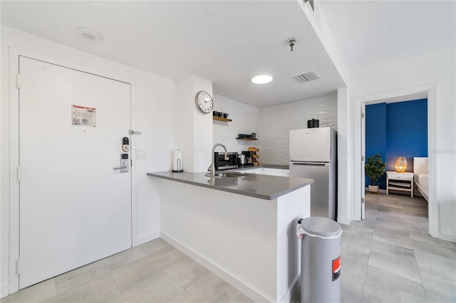 kitchen with sink, white cabinets, white refrigerator, light tile patterned floors, and kitchen peninsula