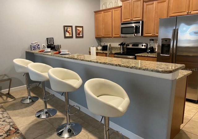 kitchen with stainless steel appliances, light stone countertops, a breakfast bar area, and light tile patterned floors