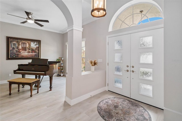 foyer featuring ornate columns, ornamental molding, ceiling fan, light wood-type flooring, and french doors