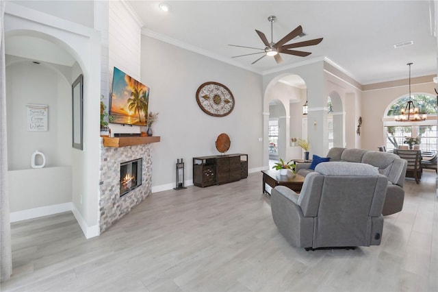 living room with ornamental molding, a fireplace, ceiling fan with notable chandelier, and light wood-type flooring