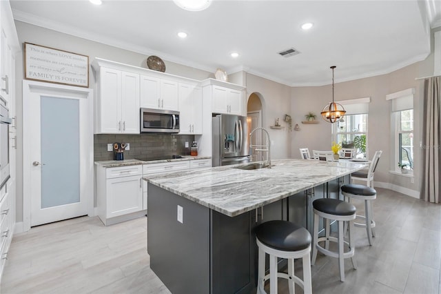 kitchen featuring appliances with stainless steel finishes, a kitchen island with sink, pendant lighting, and white cabinets