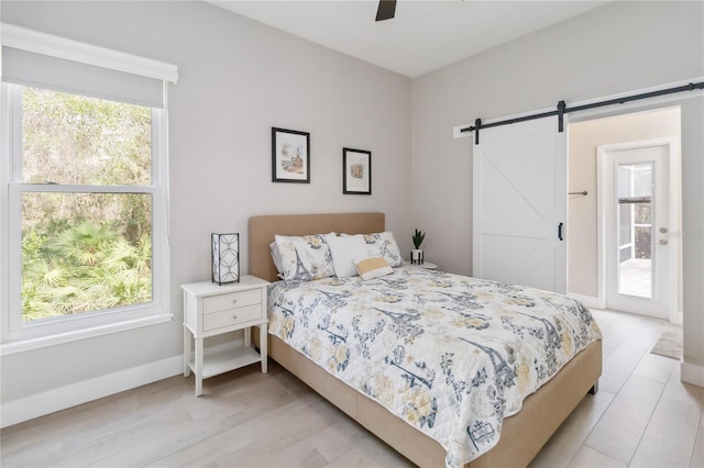 bedroom featuring ceiling fan, a barn door, access to outside, and light wood-type flooring