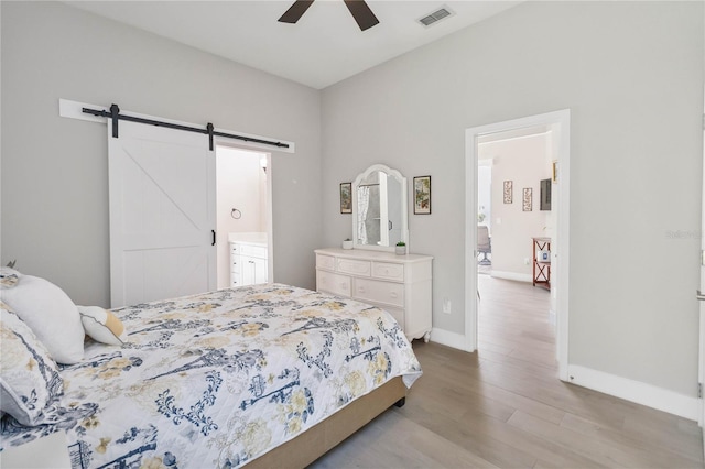 bedroom featuring ceiling fan, connected bathroom, a barn door, and light hardwood / wood-style floors