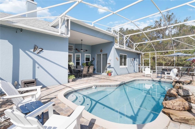 view of swimming pool with ceiling fan, glass enclosure, and a patio